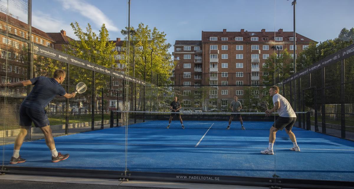 Four players in a padel match on an outdoor court in Gothenburg with brick buildings behind