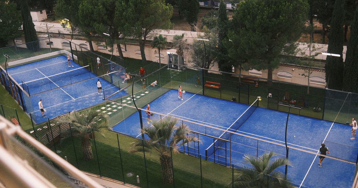 Padelspelare i match på blå banor omgivna av grönska