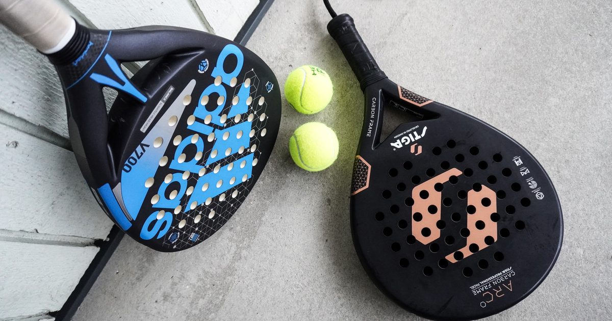 Två padelracket utan strängar och tre padelbollar ligger på ett konstgräsunderlag