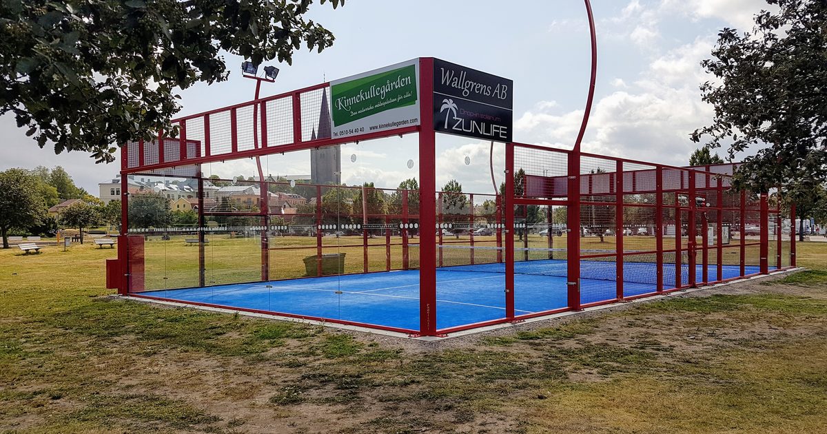 Utomhusbana för padel med glasväggar, nät och tydliga vita servelinjer på grönt underlag